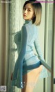 A woman in a blue sweater is posing by a window.