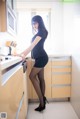 A woman in a black dress standing in a kitchen.