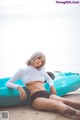 A woman sitting on top of a blue kayak on a beach.