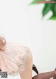 A woman in a pink dress and black stockings sitting on a white table.