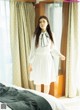 A woman in a white dress standing in front of a bed.