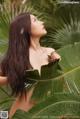 A woman with long brown hair standing in front of a palm tree.