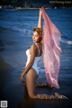 A woman in a white bathing suit holding a pink scarf.