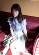 A woman sitting on a red couch wearing a blue shirt and white skirt.