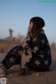 A woman sitting on a sand dune wrapped in a blanket.