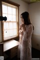 A woman in a white robe standing in front of a window.