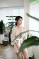 A woman in a white robe standing next to a plant.