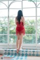 A woman in a red lingerie standing in front of a window.