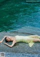 A woman in a yellow dress laying on a rock by the water.