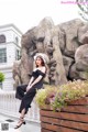 A woman in a black dress and hat sitting on a wooden planter.